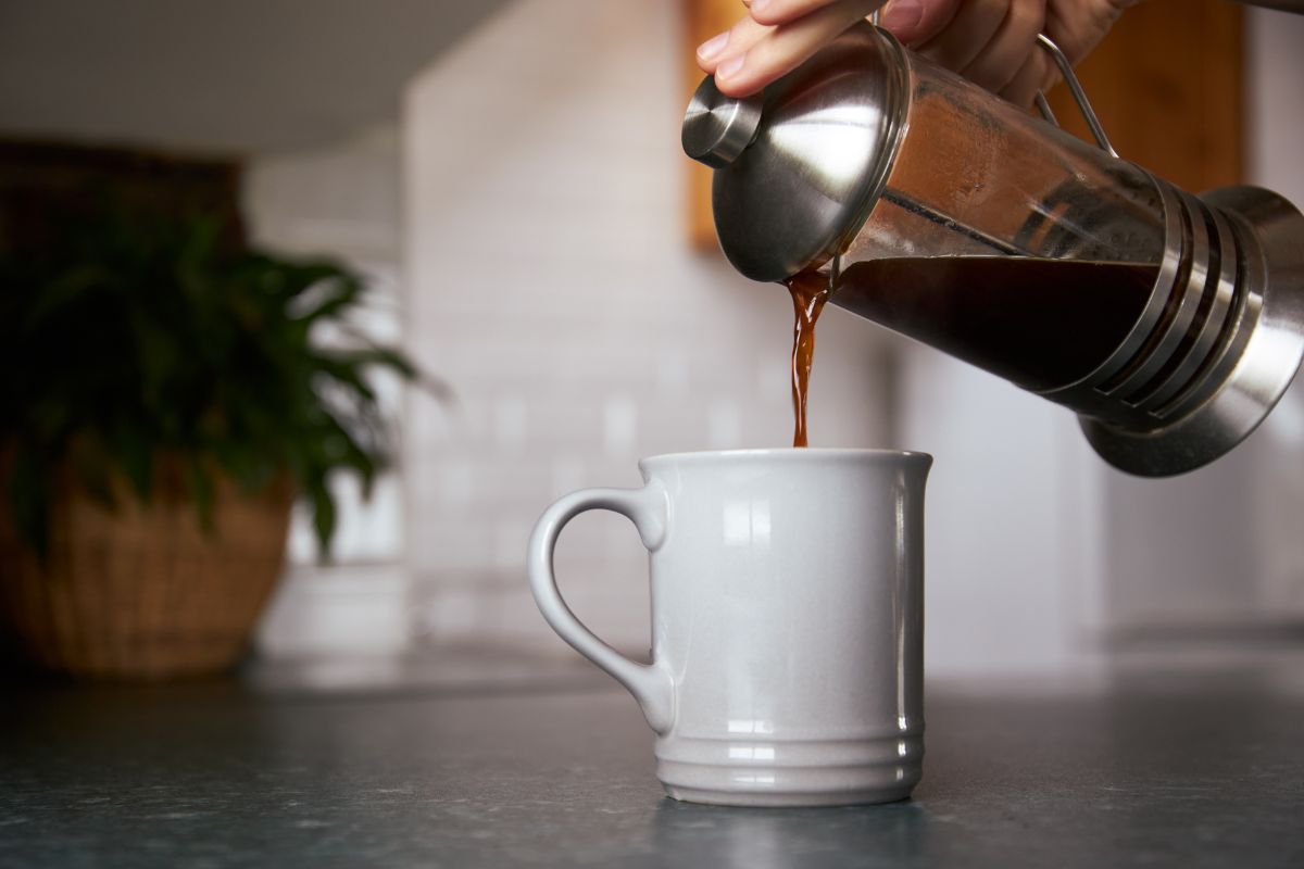 Person pouring freshly brewed coffee from a cafetière into a white ceramic mug