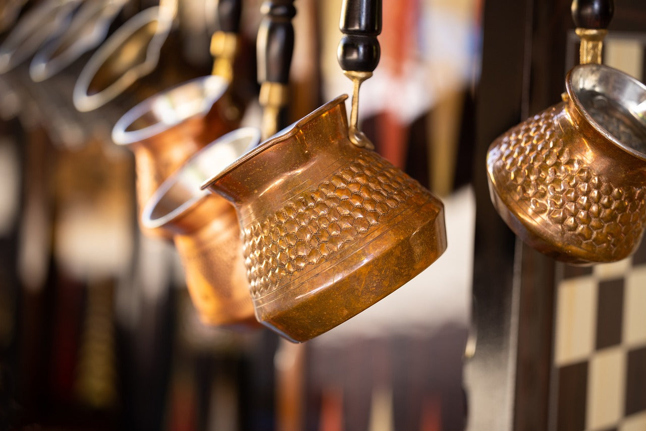 Traditional hammered copper Turkish coffee pots (cezves) hanging in a row with black handles.
