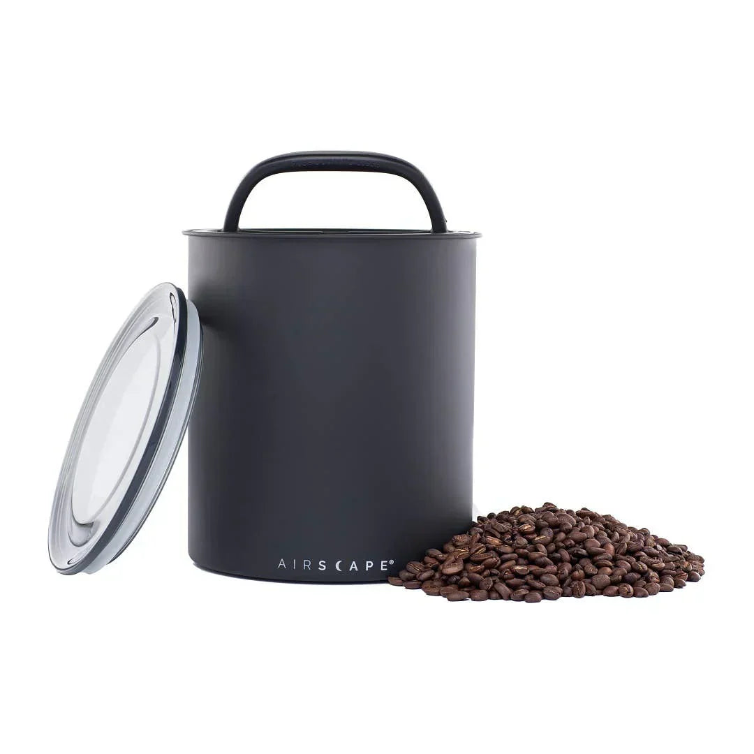 Matte black Airscape Classic coffee storage canister with airtight lid, shown with whole roasted coffee beans spilled beside it.